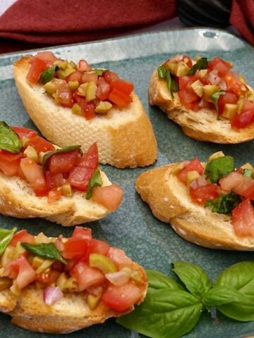Five servings of bruschetta on a plate of vegetarian finger foods.
