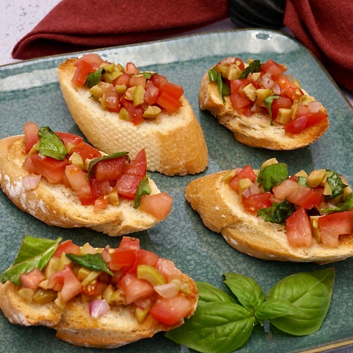 Five servings of bruschetta on a plate of vegetarian finger foods.