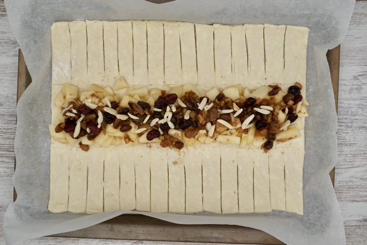A rectangular sheet of pastry with a line of fruit and nut filling for apple strudel.