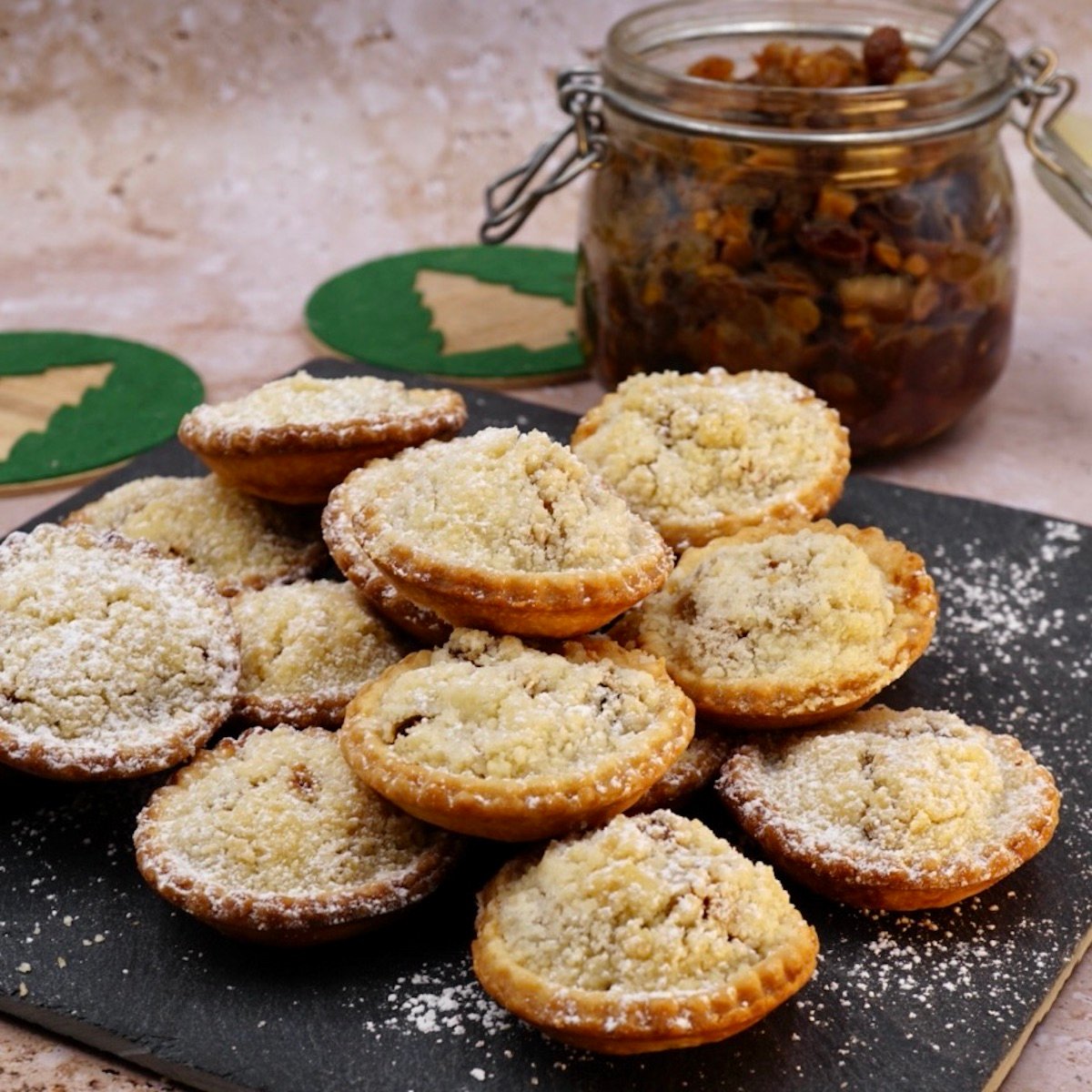 A pile of crumble topped mince pies next to a jar of mincemeat.