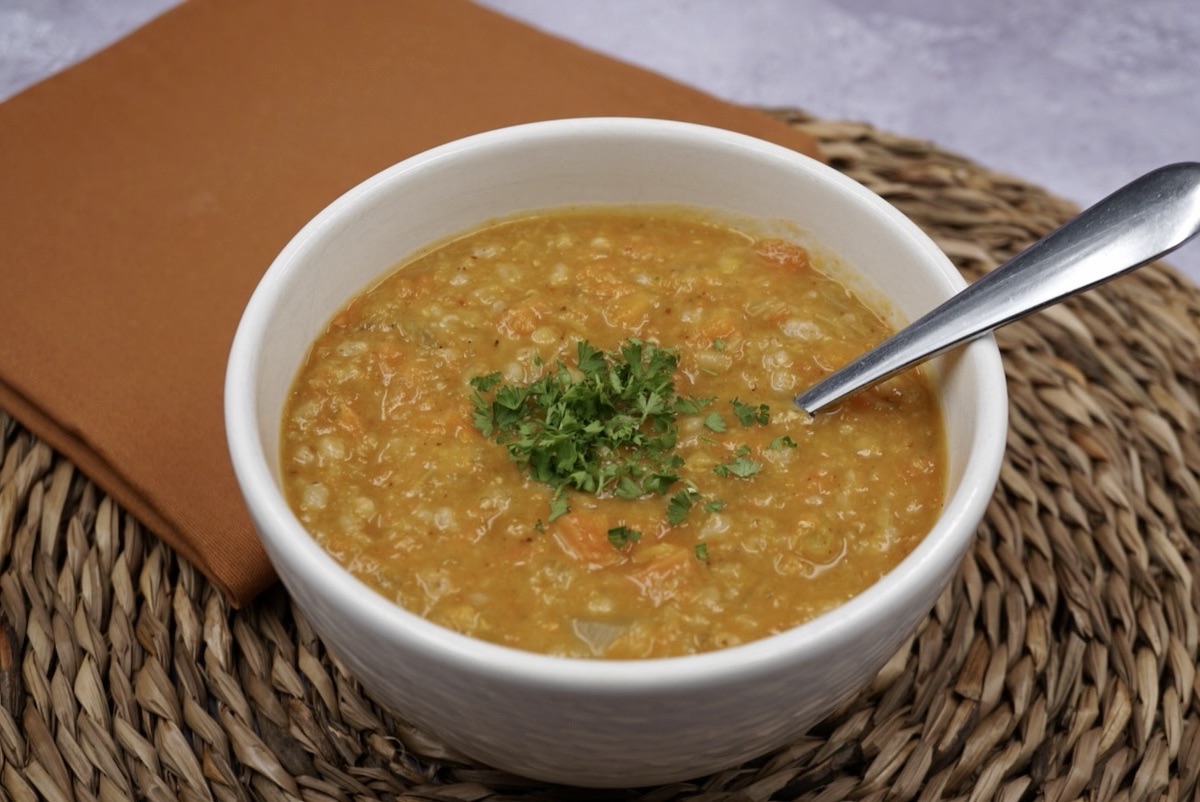 A bowl of winter vegetable soup with a spoon and parsley garnish.