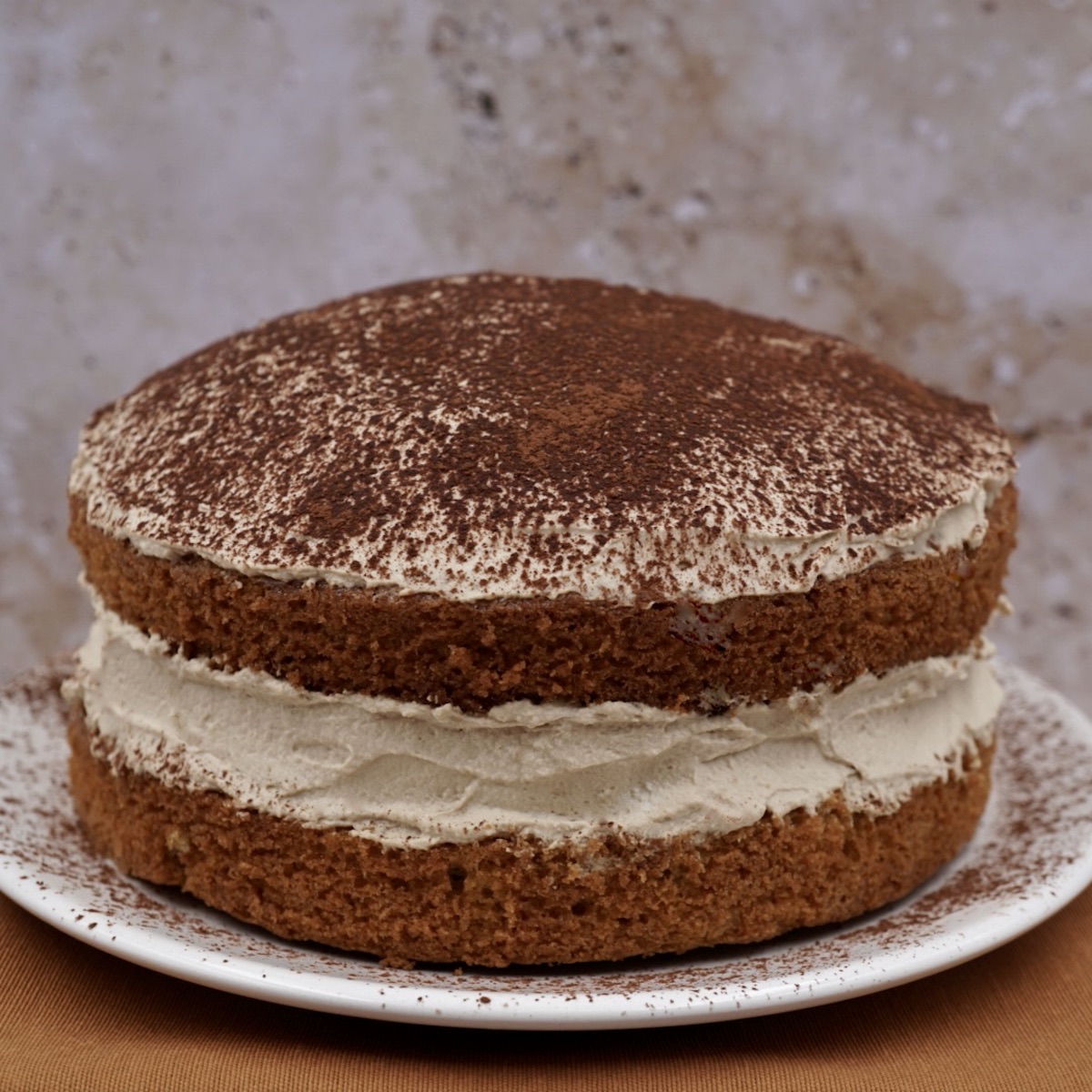 An espresso coffee sponge cake with frosting and a dusting of cocoa powder. 