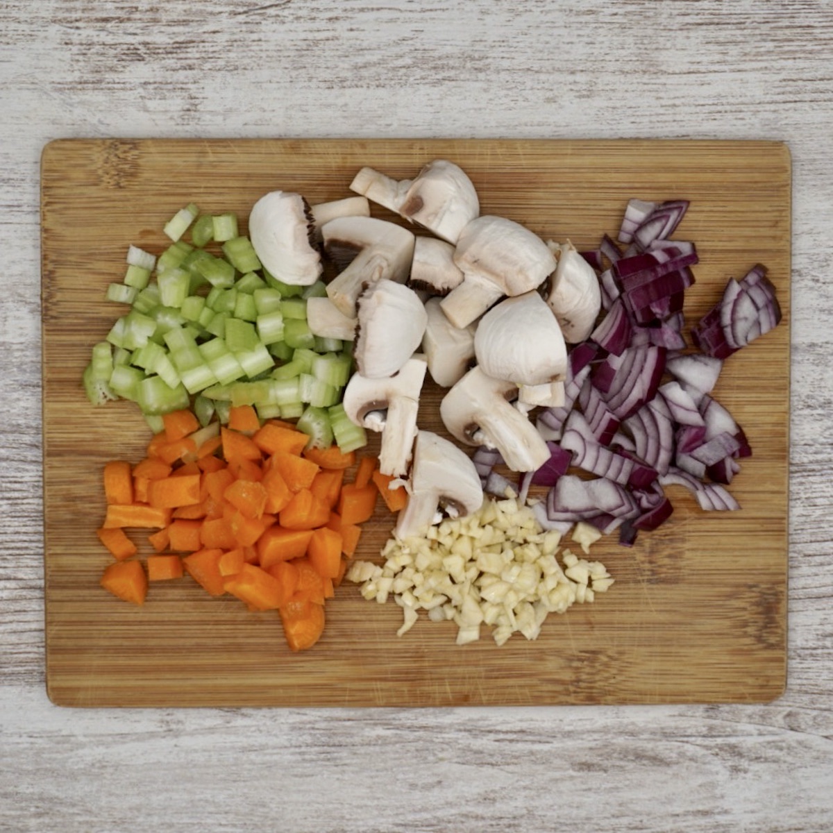 Chopped celery, mushrooms, onion, carrot and garlic on a wooden board.