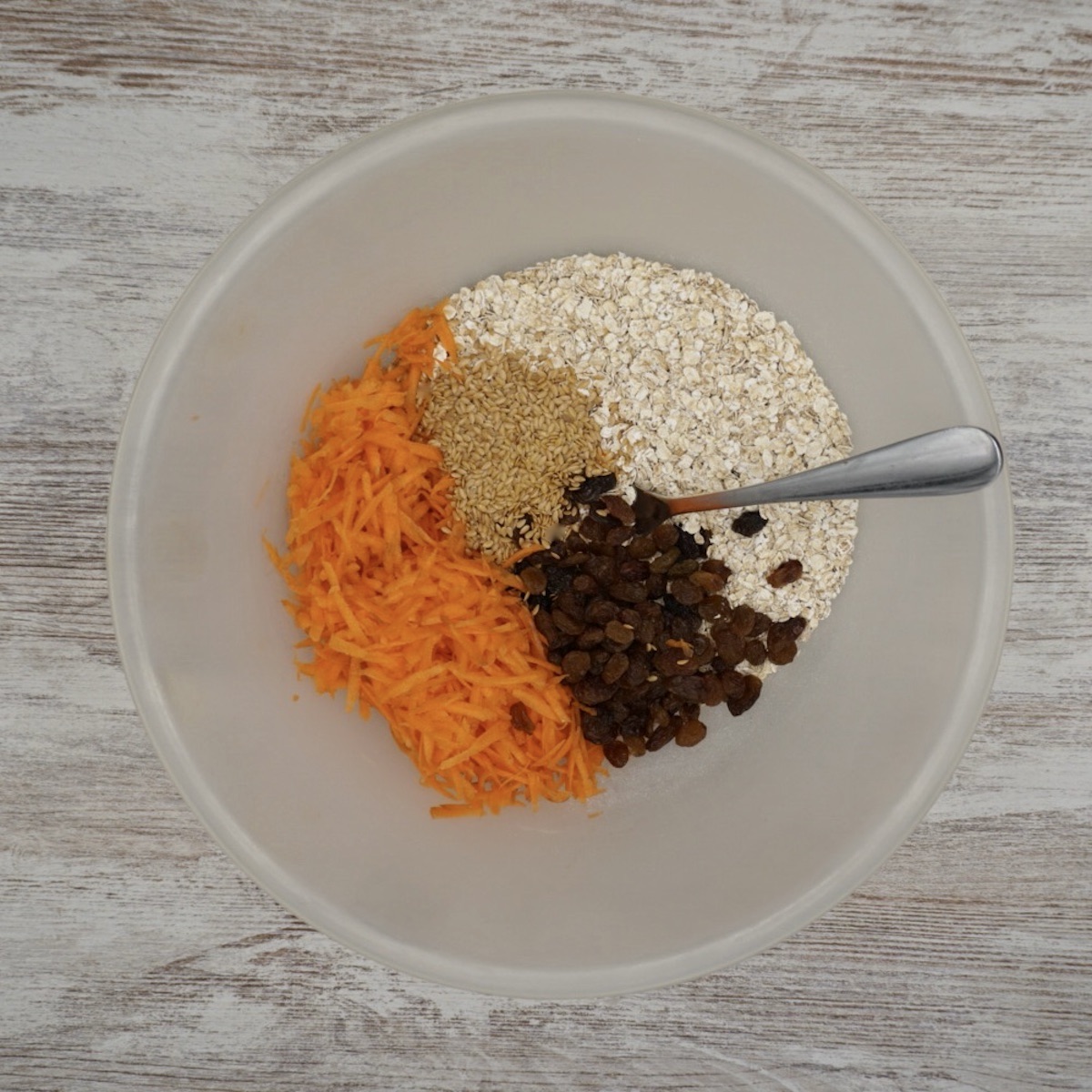 A bowl containing oats, seeds, grated carrot and raisins.