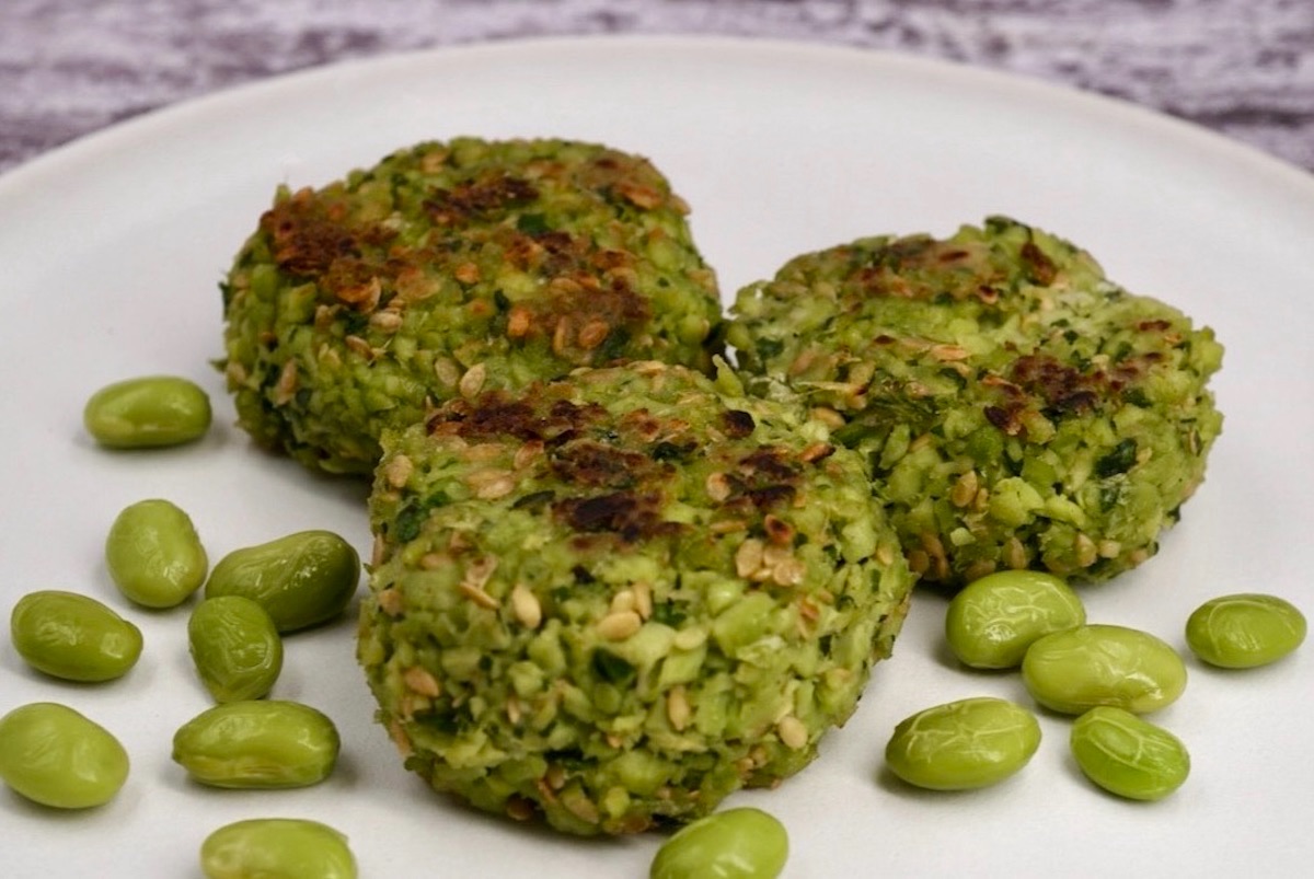 Three edamame fritters on a plate next to some edamame beans.