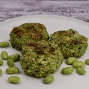 Three edamame fritters on a plate next to some edamame beans.