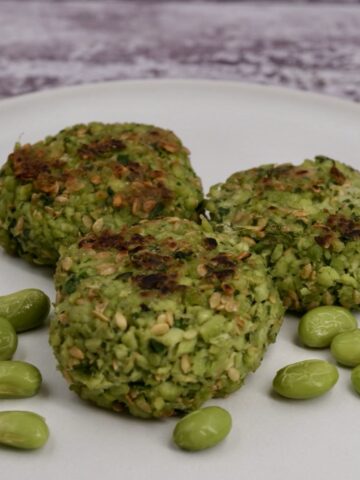 Three edamame fritters on a plate next to some edamame beans.