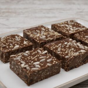 Six chocolate tahini squares decorated with seeds.