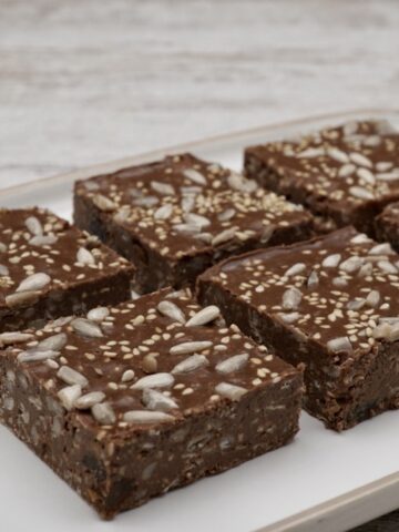 Six chocolate tahini squares decorated with seeds.