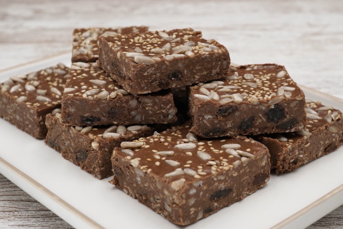 A stack of chocolate tahini squares decorated with seeds.