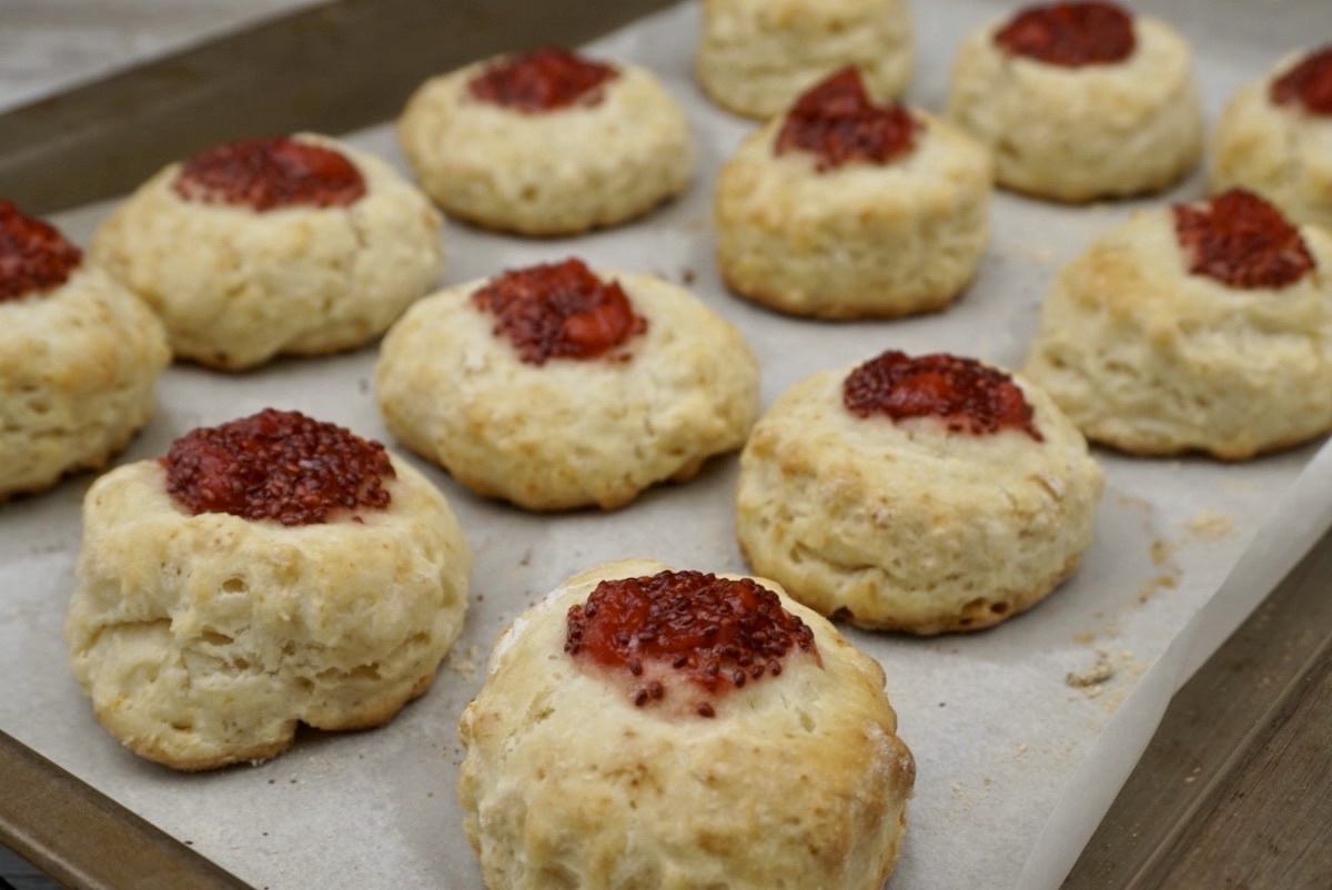 Freshly baked jam filled scones on a baking tray.
