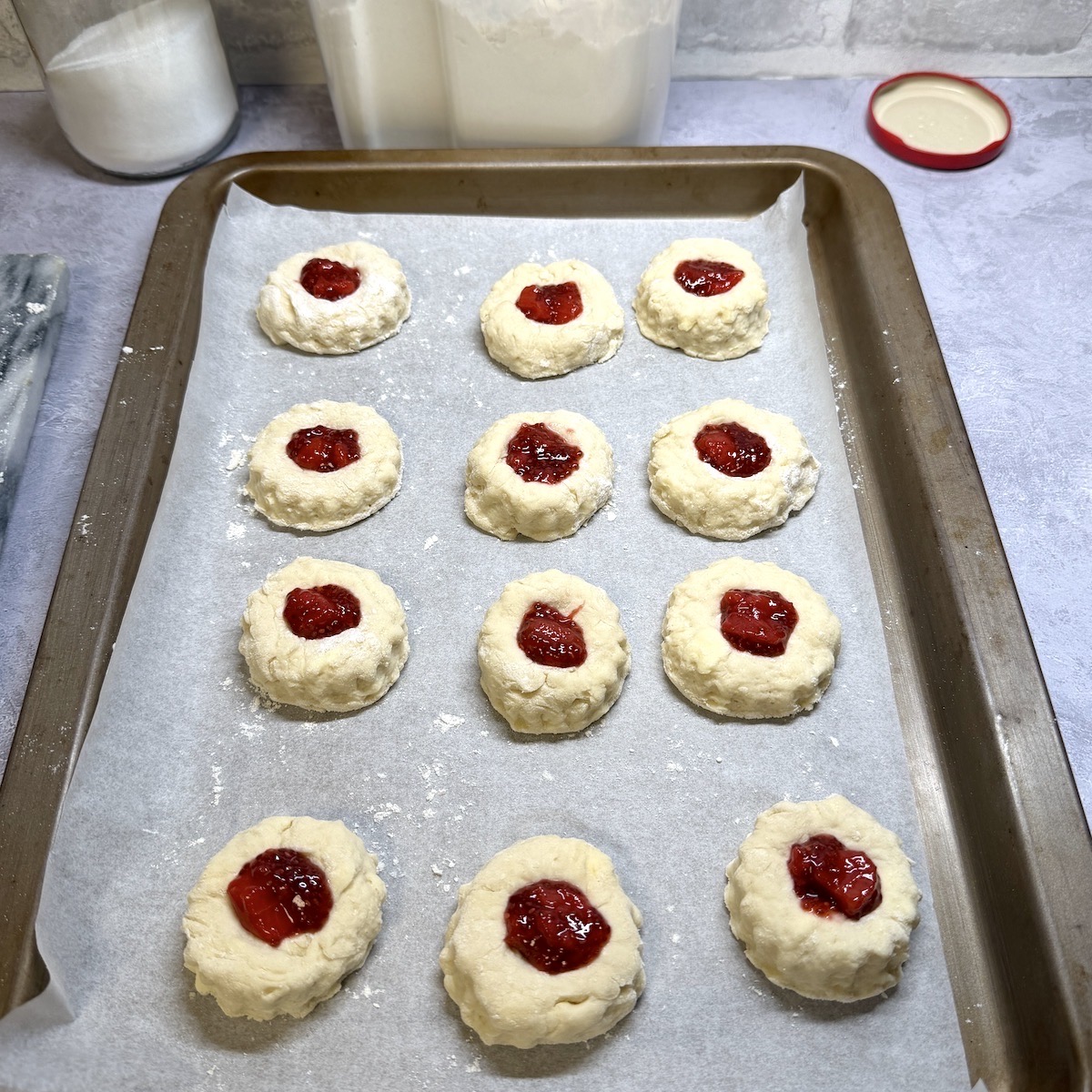 Twelve unbaked scones on a baking tray filled with jam.