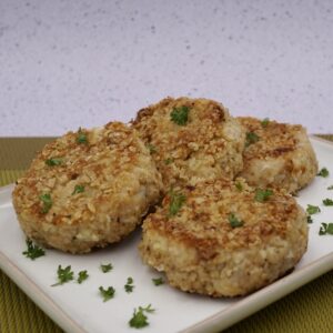 Four cauliflower cakes on a plate with herb garnish.