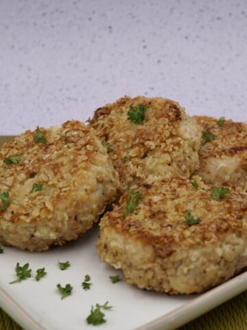Four cauliflower cakes on a plate with herb garnish.