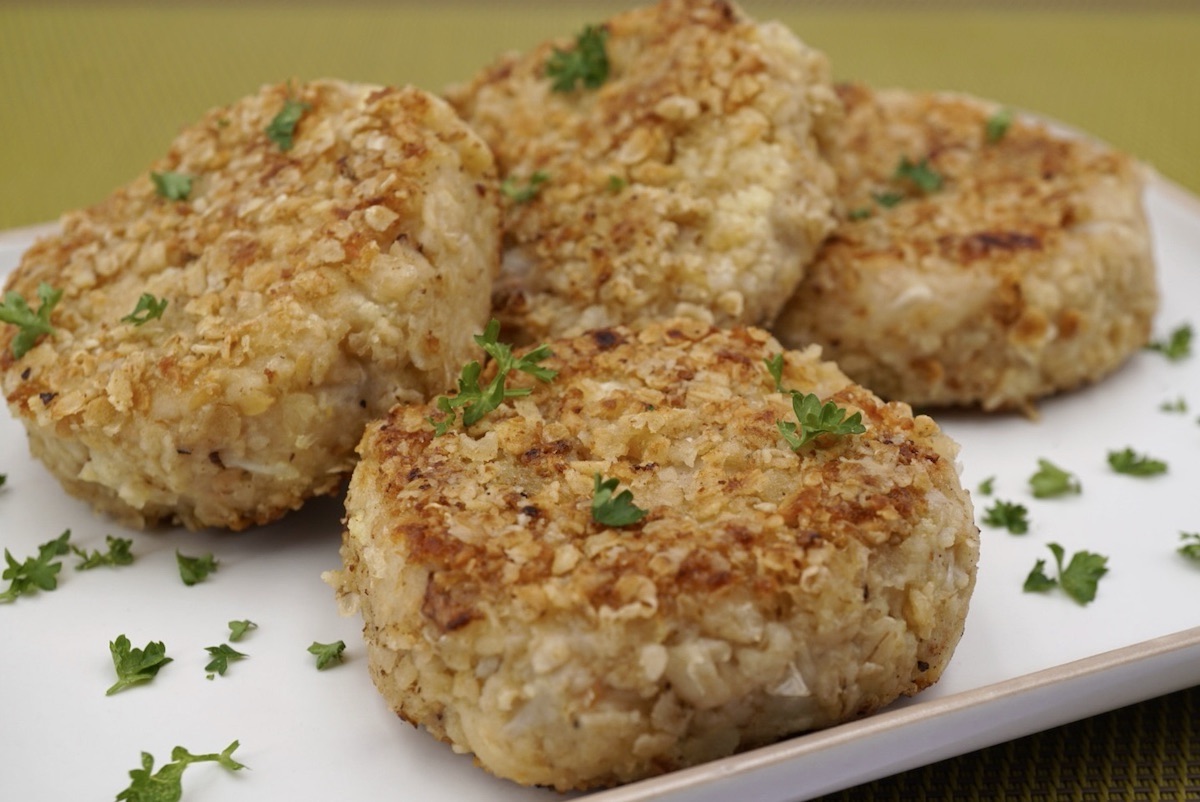 Four cauliflower cakes on a plate with herb garnish.