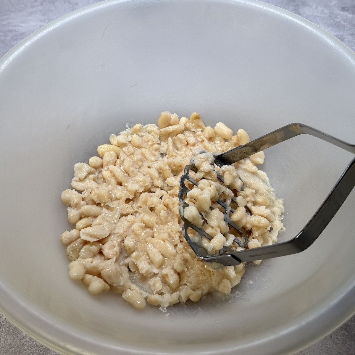 White beans in a bowl being mashed.